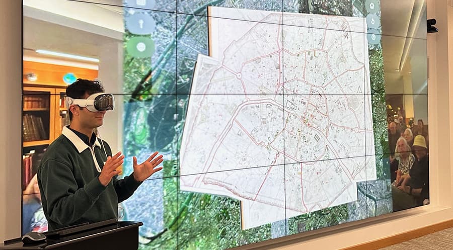 Person demonstrating a VR headset with a map image projected on a screen behind them.