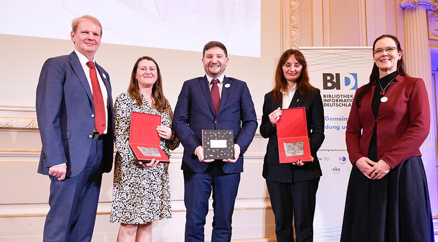 People standing on a stage at an awards ceremony displaying the medals received.